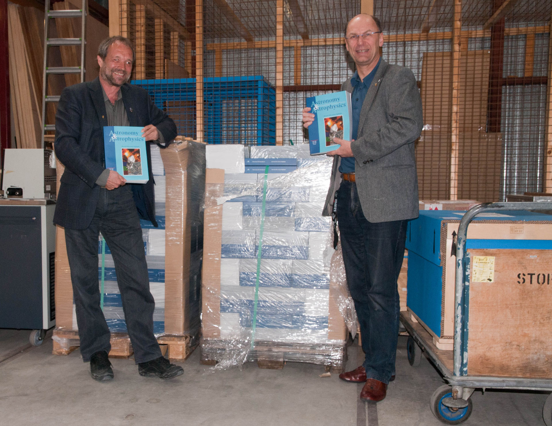 Johannes Riedinger and Göran Pilbratt stand in front of the Herschel A&A special issue supply in ESTEC Stores