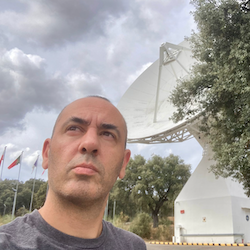 JB looking seriously into the sky with a radiotelescope antenna behind him